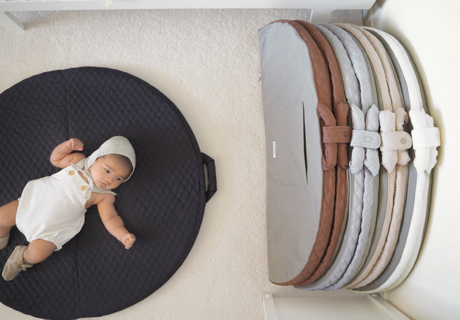 Quilted padded baby mats in earthy tones lined up against a wall with one mat open with baby laying on top of it